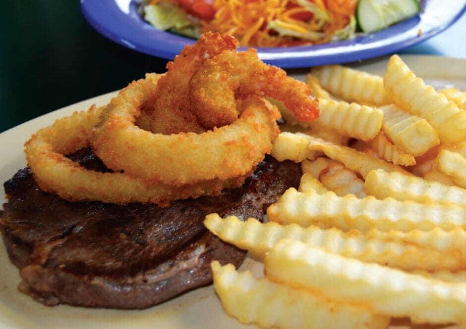 A Saturday special at Campus Drive-in featuring a 8-ounce ribeye with two onion rings, two fried shrimp, and fries.